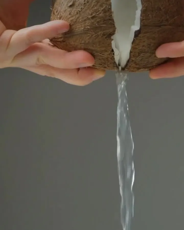 Hands cracking open a coconut, milk pouring out